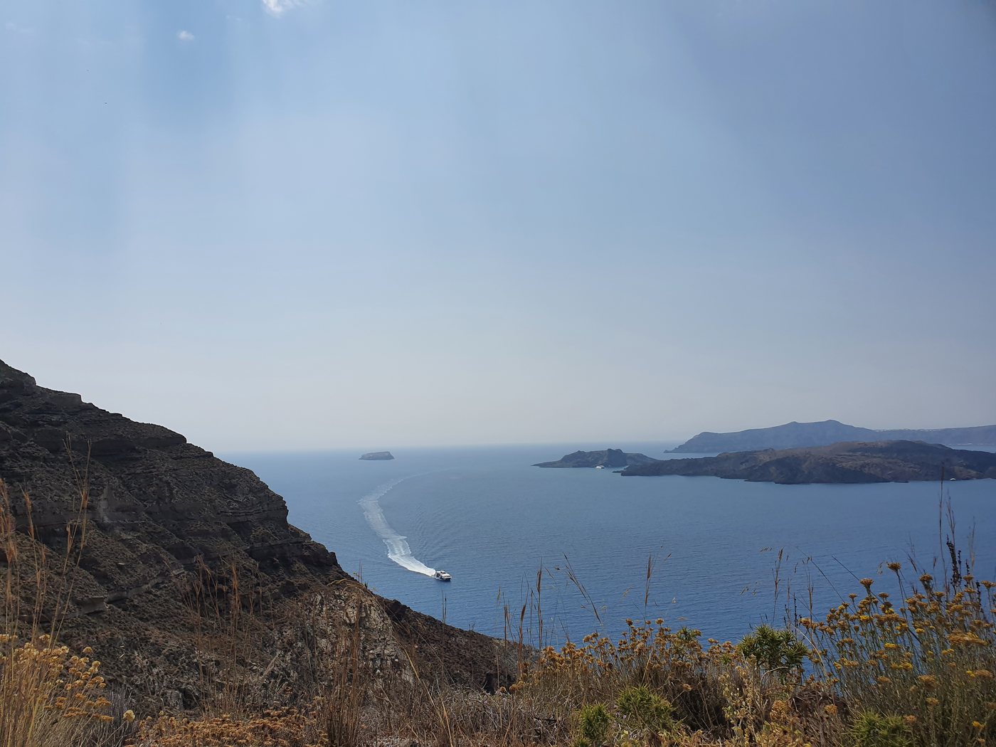 A high-speed ferry crossing the Santorini caldera, seen from the cliff road above Athinios