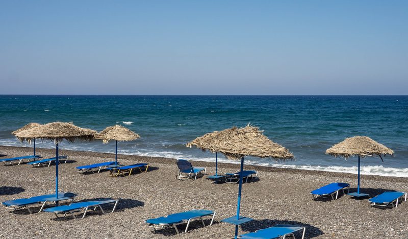 A serene Kamari Beach in Santorini with clear blue waters and a sandy shoreline.