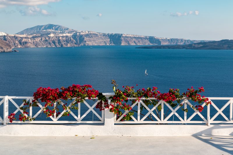 A white railing with a view of the Aegean Sea in Ia, Santorini, Greece.