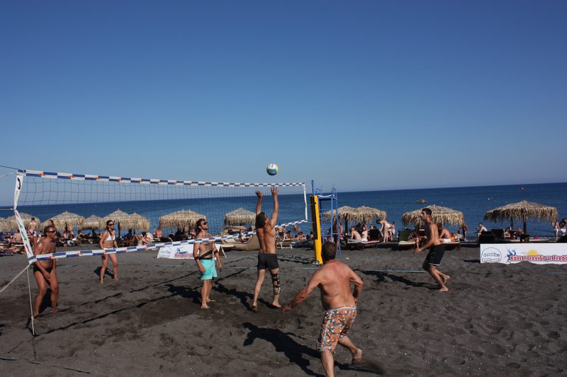 People playing beach volleyball on the sandy shore of Perivolos Beach, Santorini.