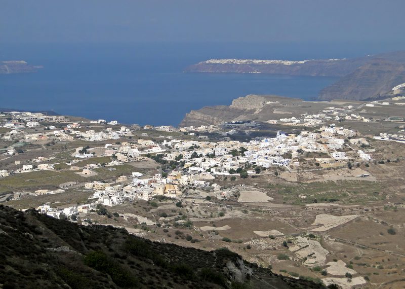 Aerial view of Pyrgos Village with whitewashed buildings and blue domes on Santorini, Greece.