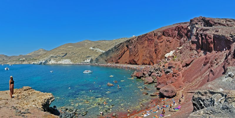 A vibrant red sand beach with dramatic cliffs in Santorini, Greece.