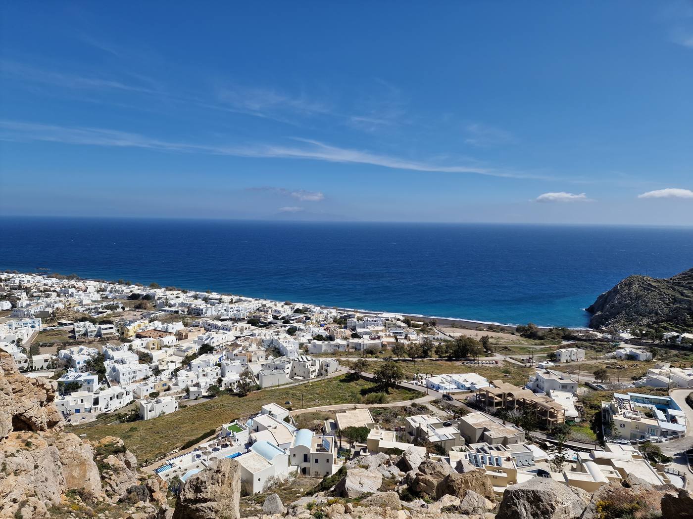 Kamari's black sand beach and whitewashed town seen from the hiking trail above, with the rocky Mesa Vouno headland in the distance