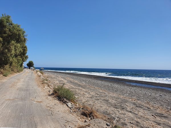 The flat black sand beach at Monolithos on Santorini's east coast, backed by a quiet coastal road