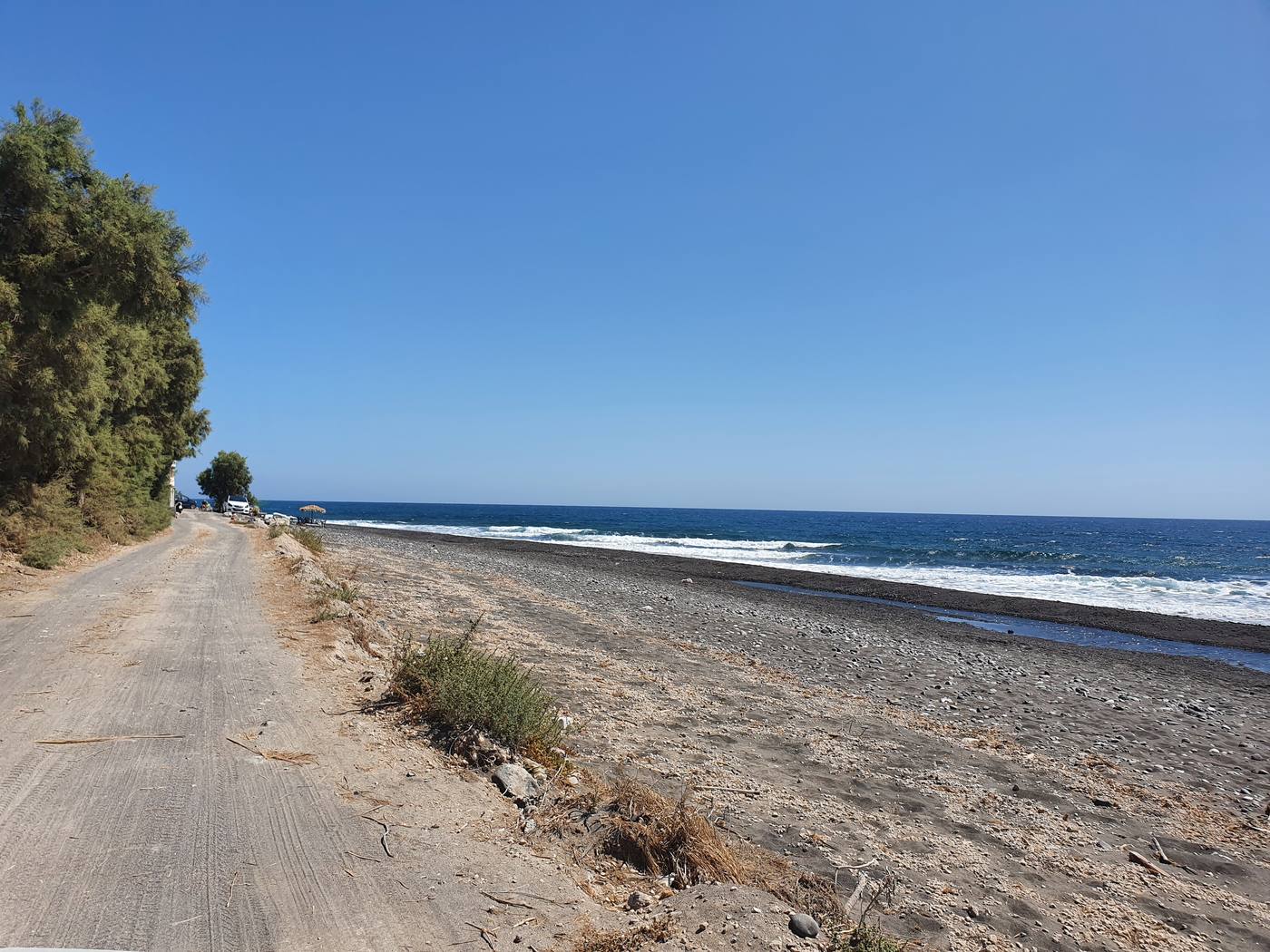 The flat black sand beach at Monolithos on Santorini's east coast, backed by a quiet coastal road