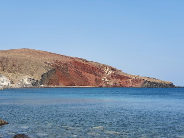 The dramatic red volcanic cliffs of Red Beach curving around the sandy cove near Akrotiri