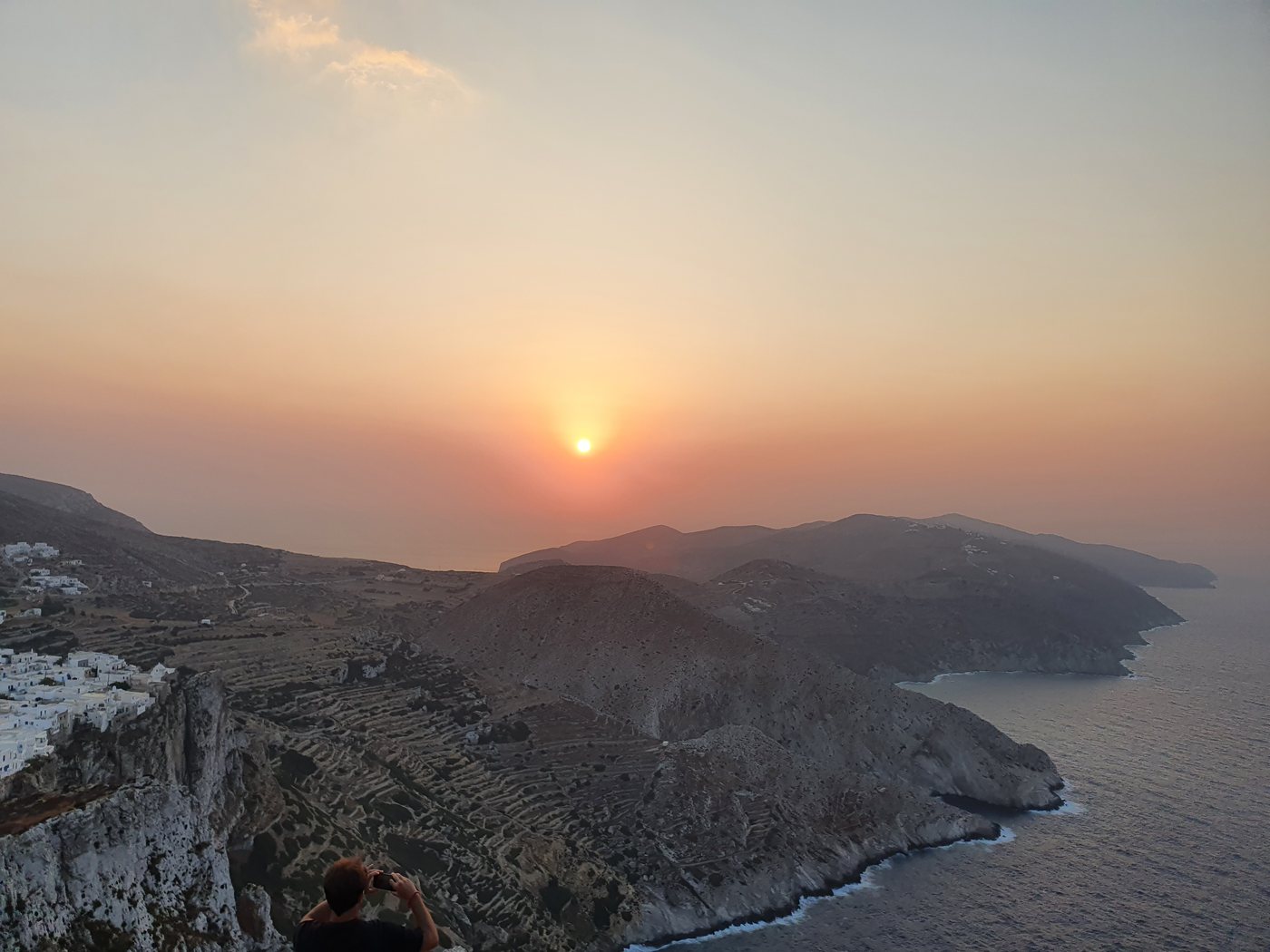 The whitewashed Chora of Folegandros perched on a sheer cliff edge above the sea at sunset